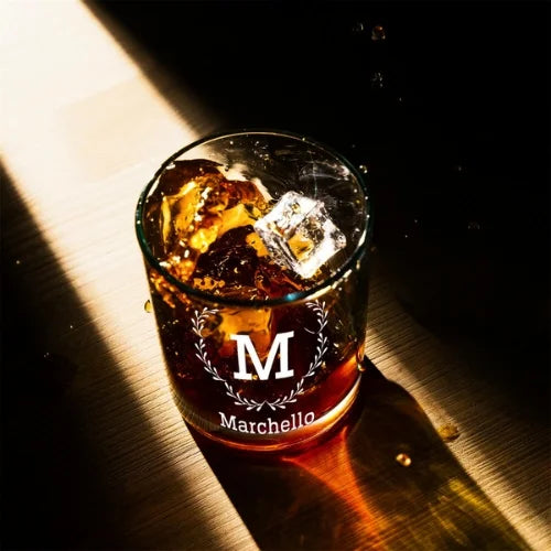Verre à whisky personnalisé 'Marchello', rempli de whisky et glaçons, capturé sous une lumière dorée mettant en valeur les détails gravés.
