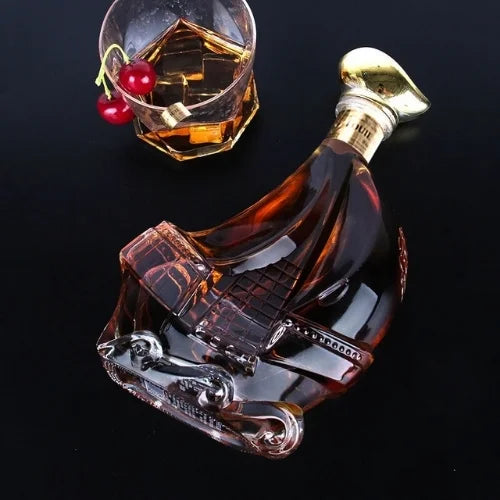 Carafe à whisky en forme de bateau vue de côté, accompagnée d'un verre de whisky et de cerises sur une table noire.