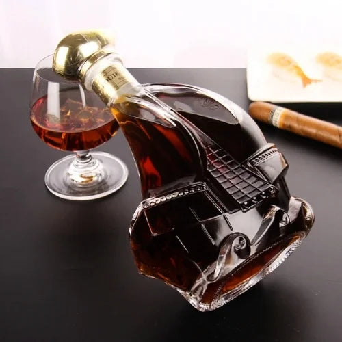 Carafe à whisky en forme de bateau inclinée sur une table avec un verre de whisky et un cigare en arrière-plan.