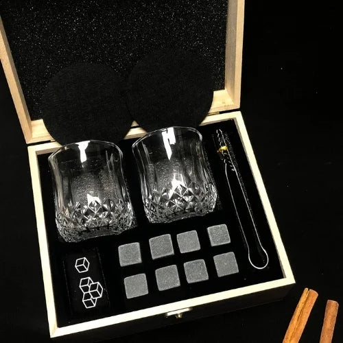 Coffret en bois raffiné contenant des verres à whisky texturés et des pierres réfrigérantes, avec des accessoires élégants, posé sur fond noir.