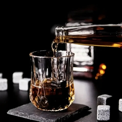 Whisky ambré versé dans un verre à whisky avec glaçons réutilisables, sur fond noir avec pierres réfrigérantes en arrière-plan.