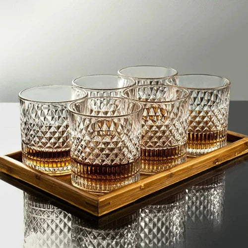 Verre à whisky en cristal texturé, rempli de whisky ambré, tenu à la main avec une lumière douce en arrière-plan pour mettre en valeur les détails du verre.