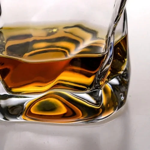 Gros plan sur les reflets dorés d’un whisky à l’intérieur d’un verre au design irrégulier et fascinant.