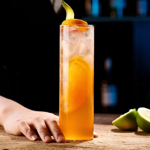 Un verre tube rempli d’un cocktail vibrant, garni de tranches d’agrumes et de zestes, prêt à égayer vos soirées.